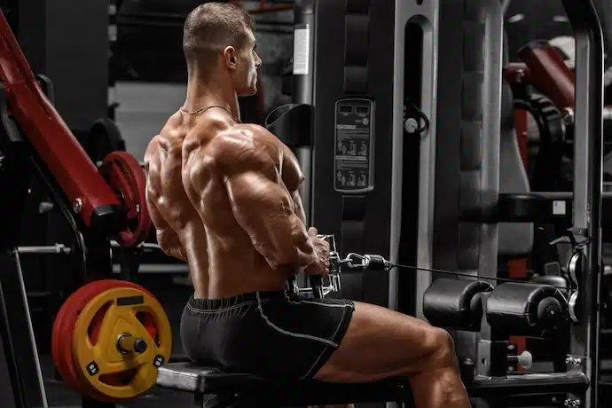 Muscular man doing cable row for back. Strong male working out in gym